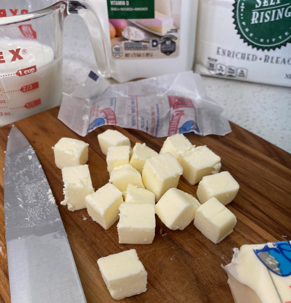 A stick of butter, cubed on a cutting board. [buttermilk biscuits]