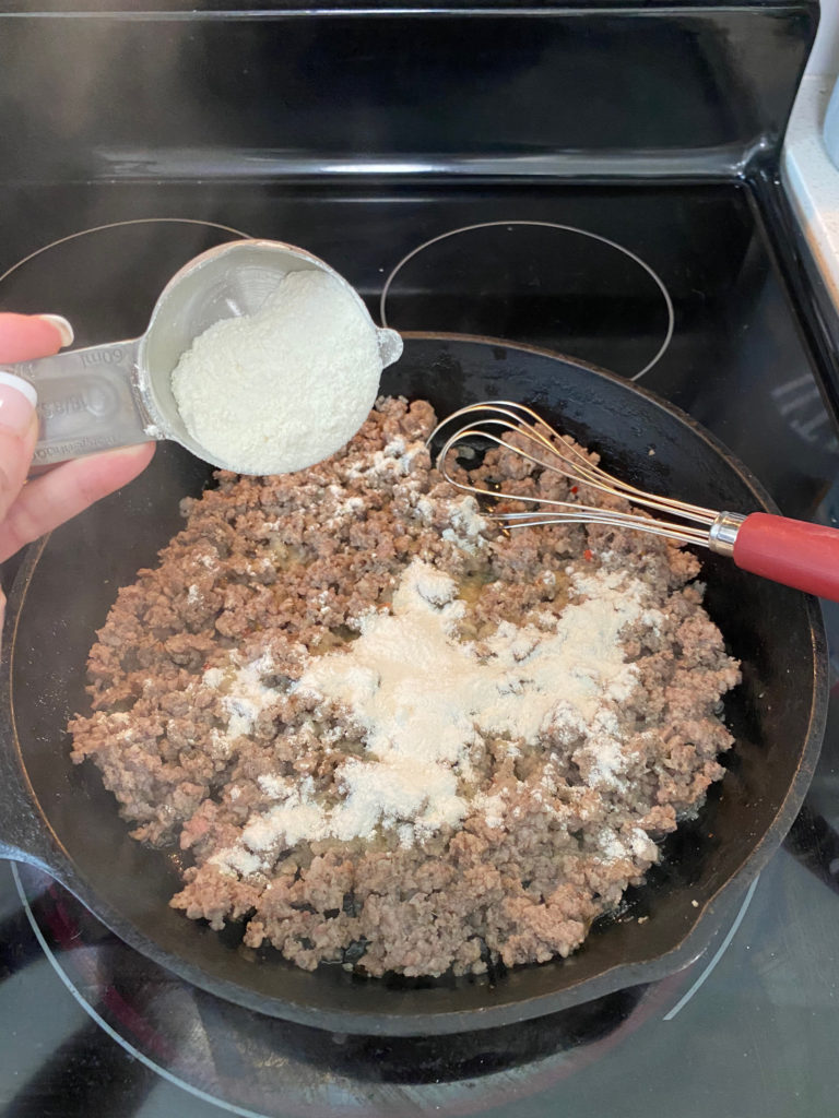 Pouring flour into the cooked sausage for biscuits and gravy. [Biscuits and Gravy]