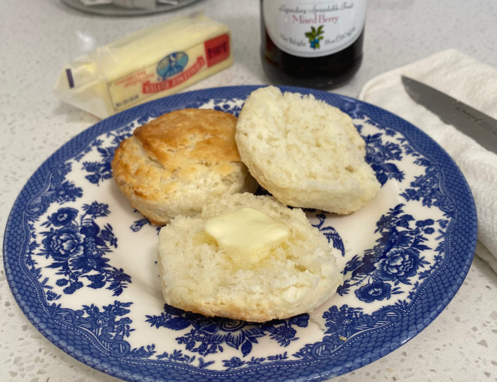 Two buttermilk biscuits on a plate, one is split open with butter on it. [buttermilk biscuits]