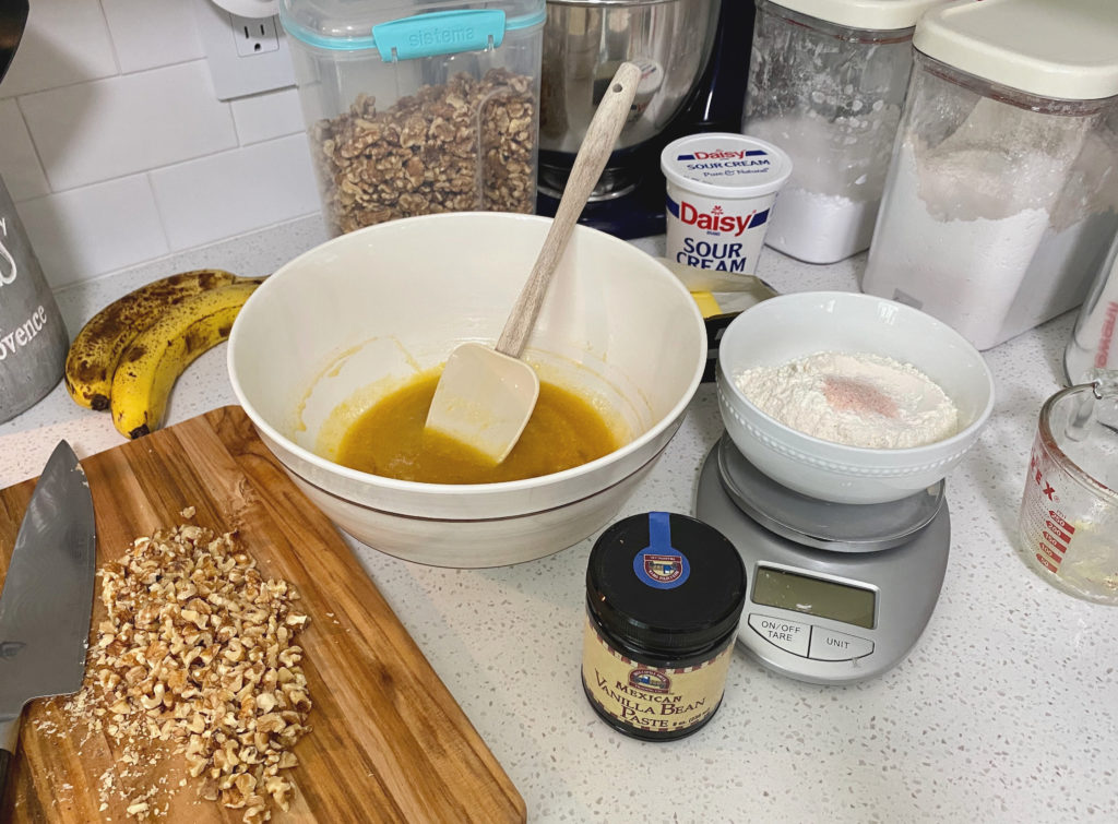 A mixing bowl and spatula on the counter surrounded by ingredients [decadent banana bread]