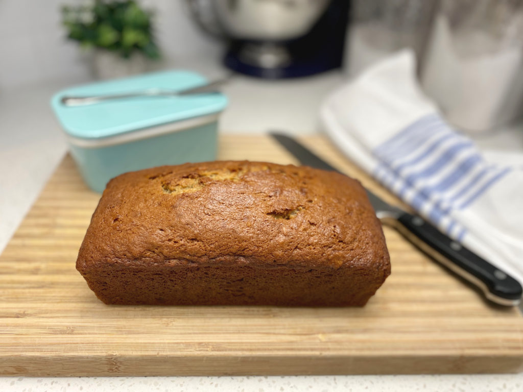 A loaf of banana bread on a cutting board with a bread knife. [decadent banana bread]