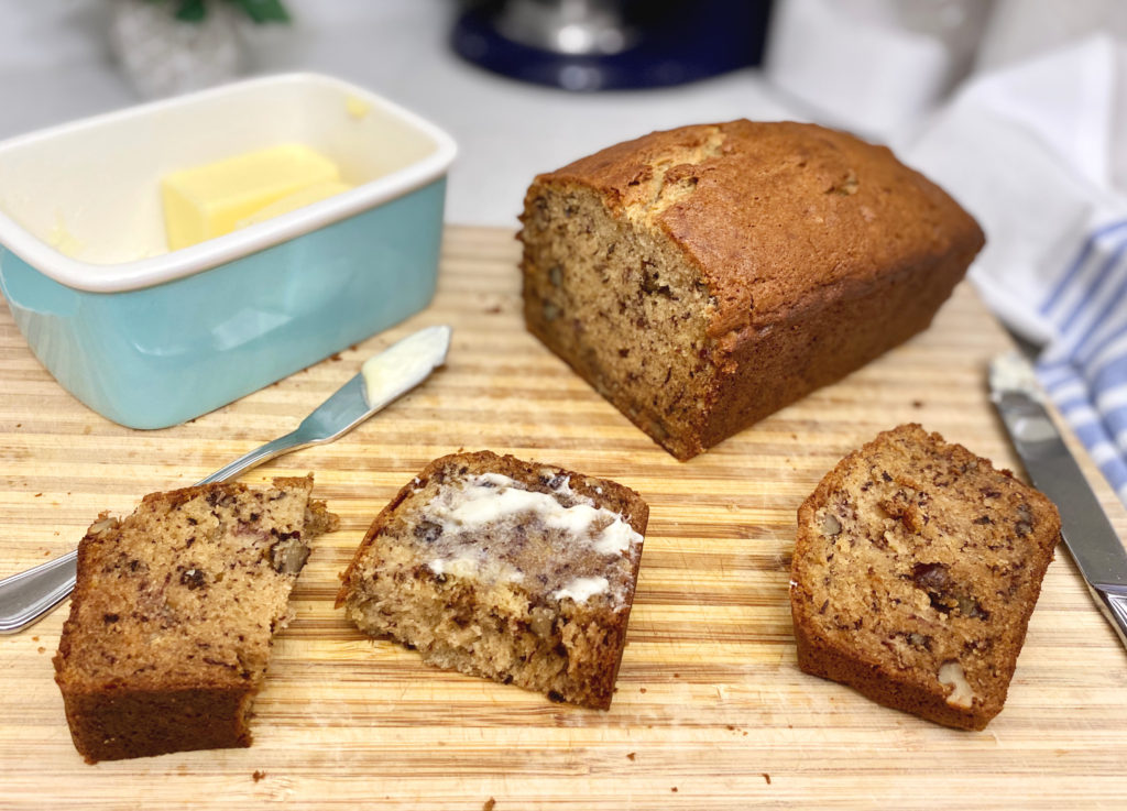 A piece of buttered banana bread on a cutting board. [decadent banana bread]