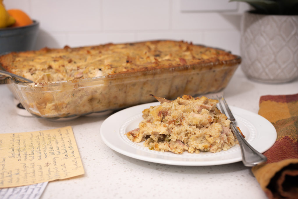 A pan of dressing in the background with a plate of dressing in front with a fork. [Chicken and Dressing]