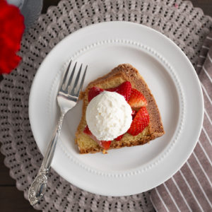 A slice of poundcake on a plate with strawberries and homemade whipped cream on top. [Strawberry Shortcake]