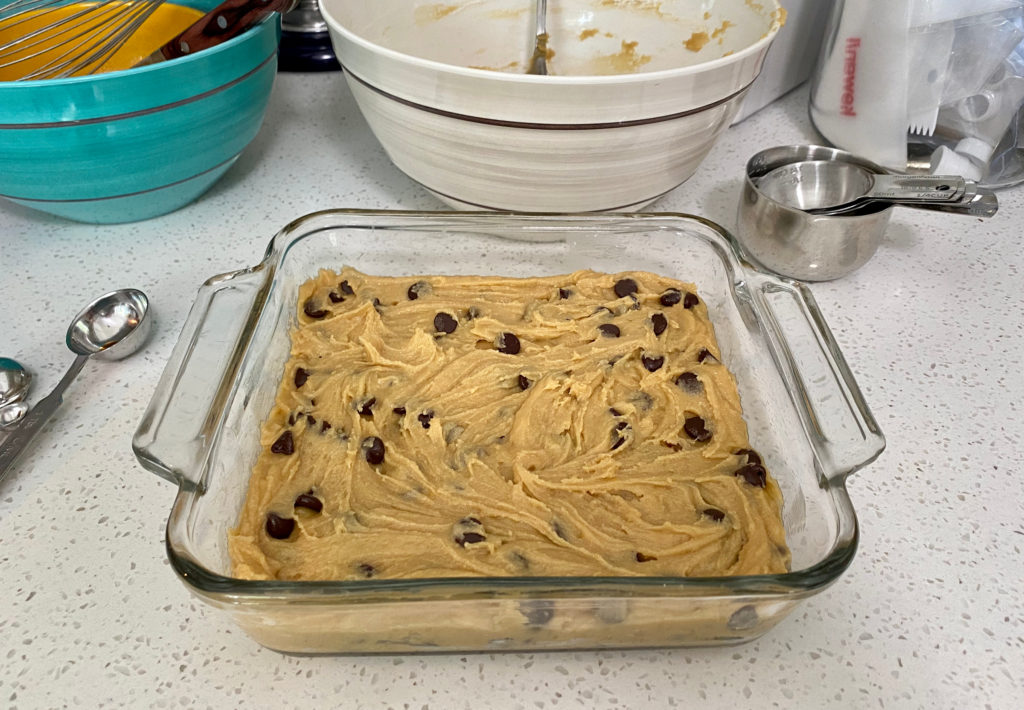 Uncooked batter in a glass 8x8 baking dish. [chocolate chip cookie bars]