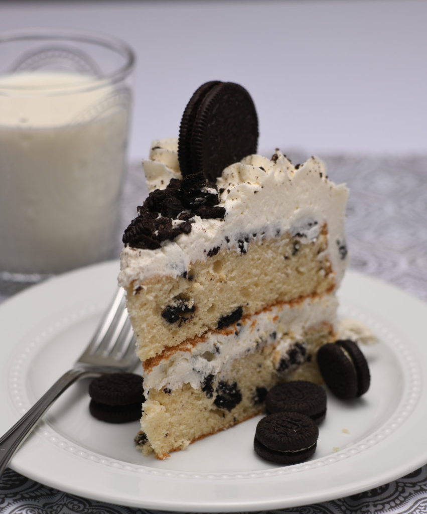 A close up view of a slice of cookies and cream cake with a glass of milk beside it. (how to make cookies and cream cake)