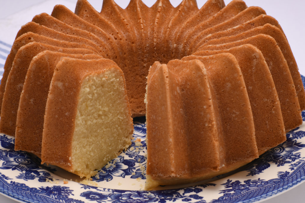 A whole pound cake on a blue patterned plate with a slice taken out. [Perfect Pound Cake]