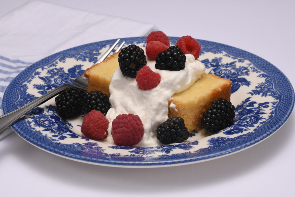 A slice of pound cake on a blue plate with whipped cream and berries on top. [Perfect Pound Cake]