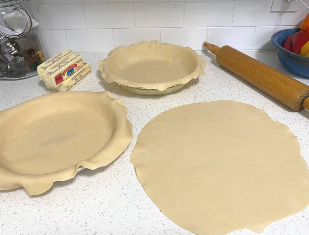 Pie dough rolled out on the counter with two pie pans and a rolling pin in the background. [Classic Chicken Pot Pie]