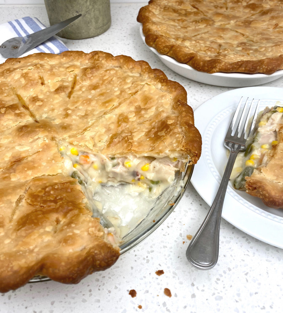 A whole pie with a slice cut out sitting on a plate with a fork. [Classic Chicken Pot Pie]