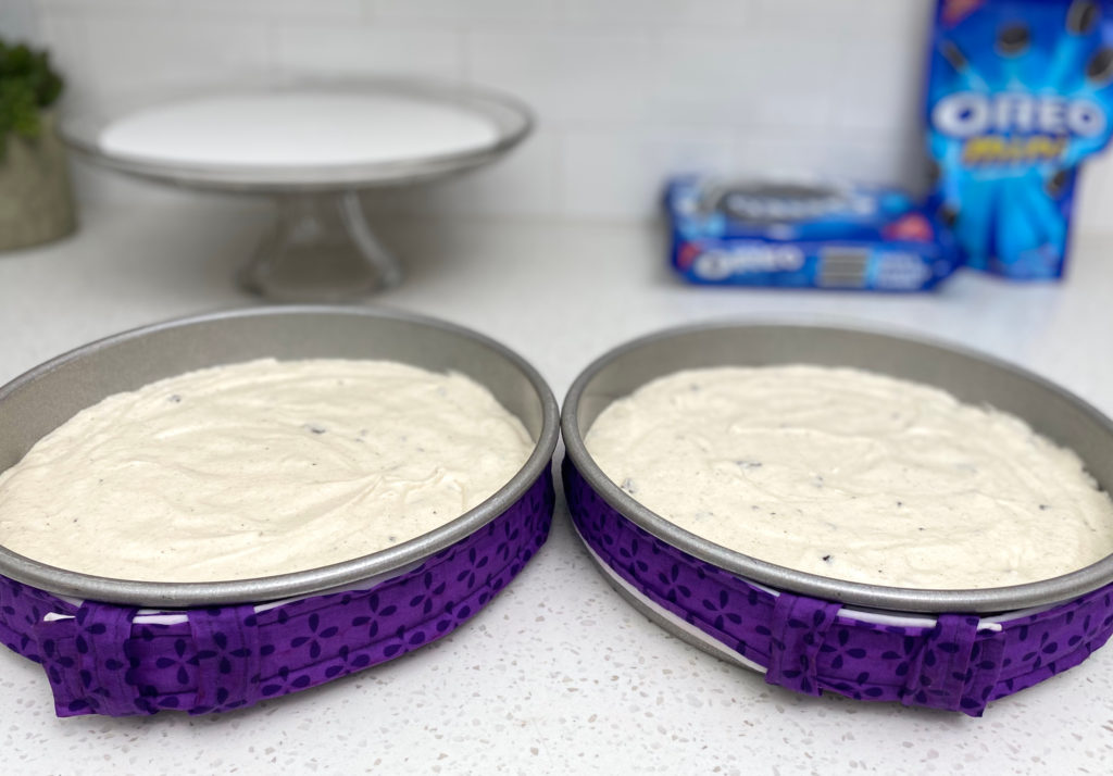 Two cake pans on a counter filled with cake batter [cookies and cream cake]