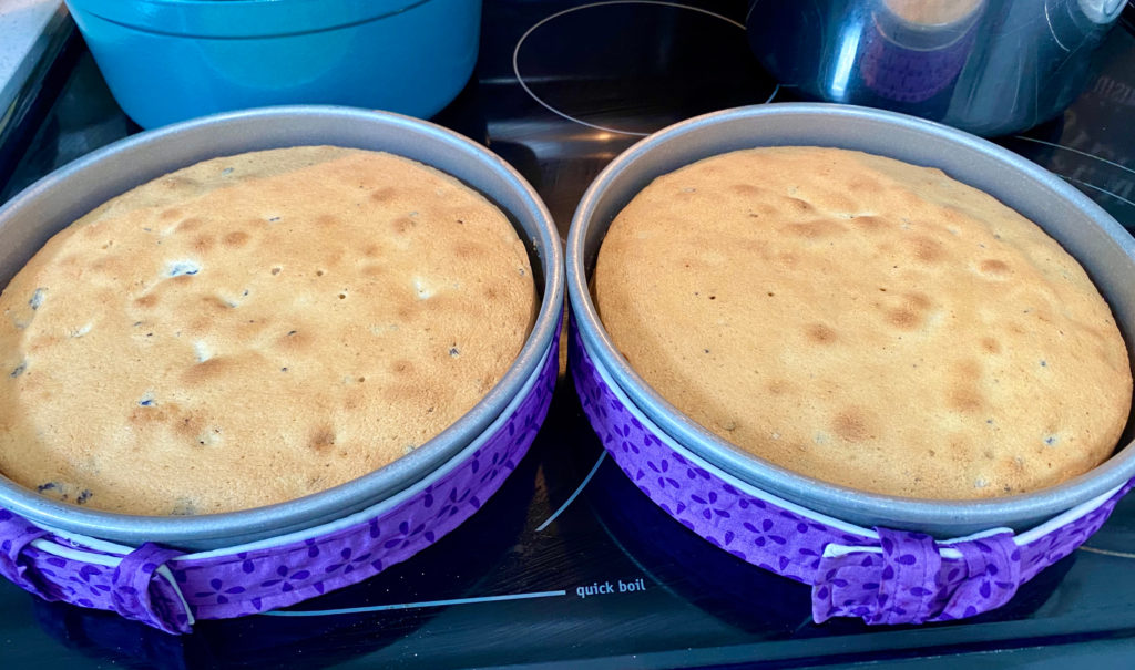 Two cake pans on a stove top with baked cakes and baking strips. (how to make cookies and cream cake)