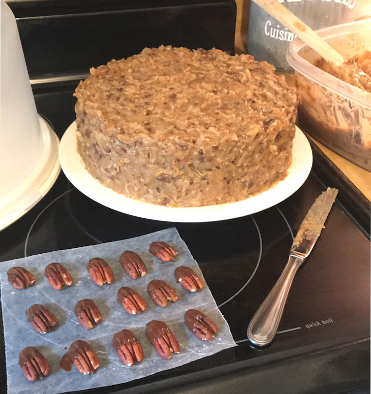 Frosted German chocolate cake on a plate with chocolate covered pecans on parchment paper, [german chocolate cake]