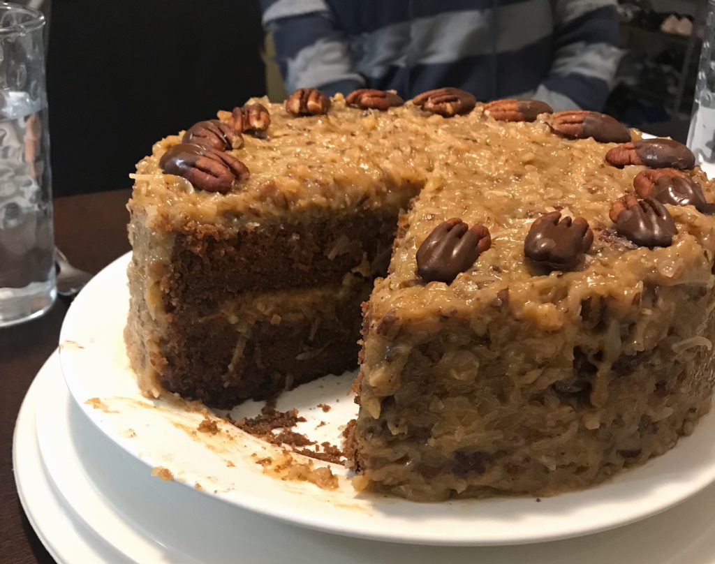 chocolate cake with coconut pecan frosting with a slice taken out. [german chocolate cake