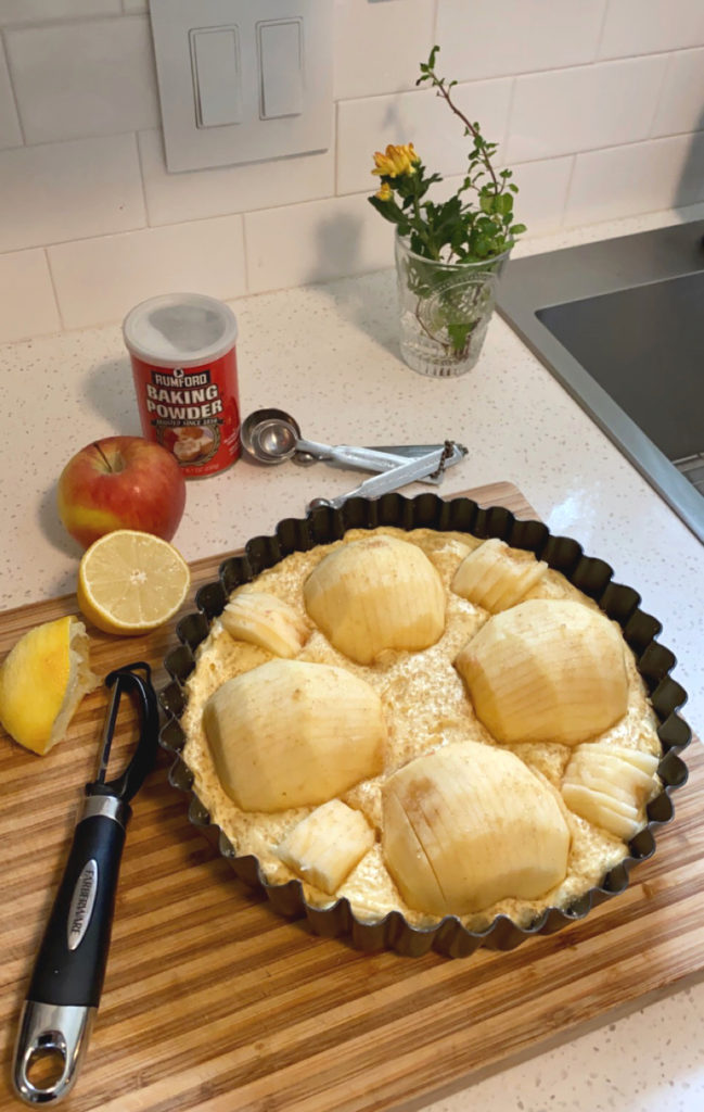 A tart tin filled with cake batter and raw apple quarters. [Sunken apple cake]