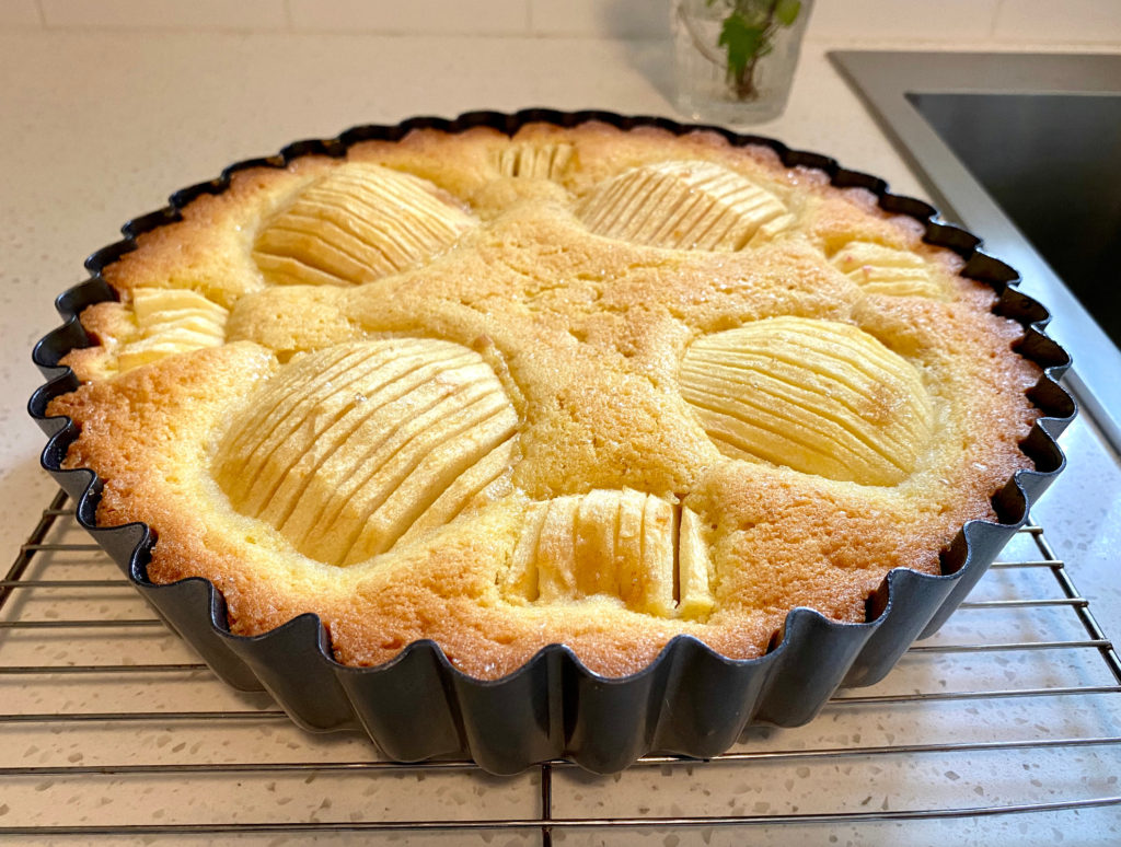 A baked cake in a tart tin cooling on a wire rack [sunken apple cake]