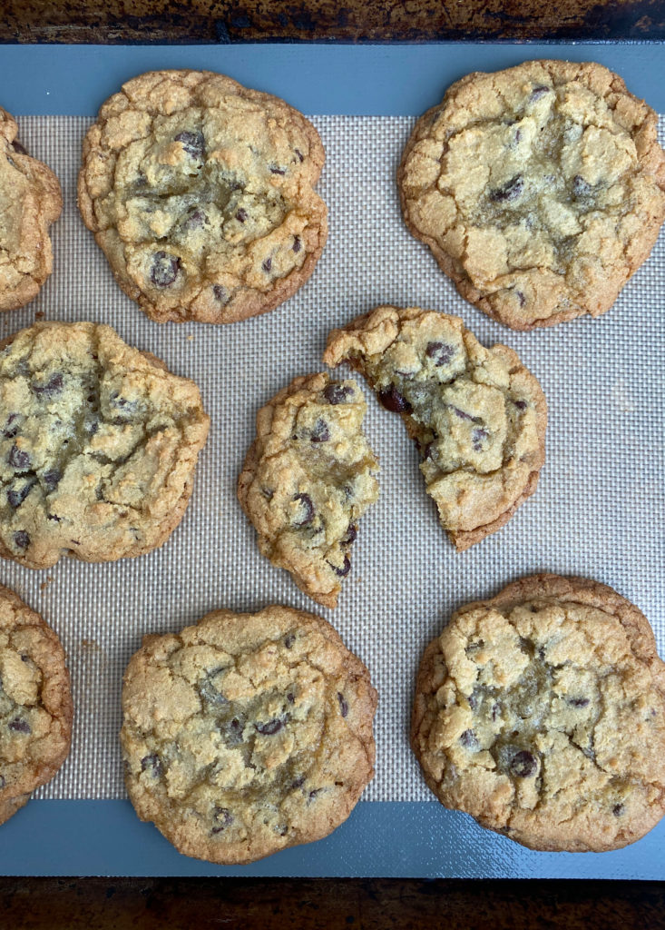 A bakoing sheet filled with freshly baked chewy chocolate chip cookies, with one cookie broken in half to show its gooey center