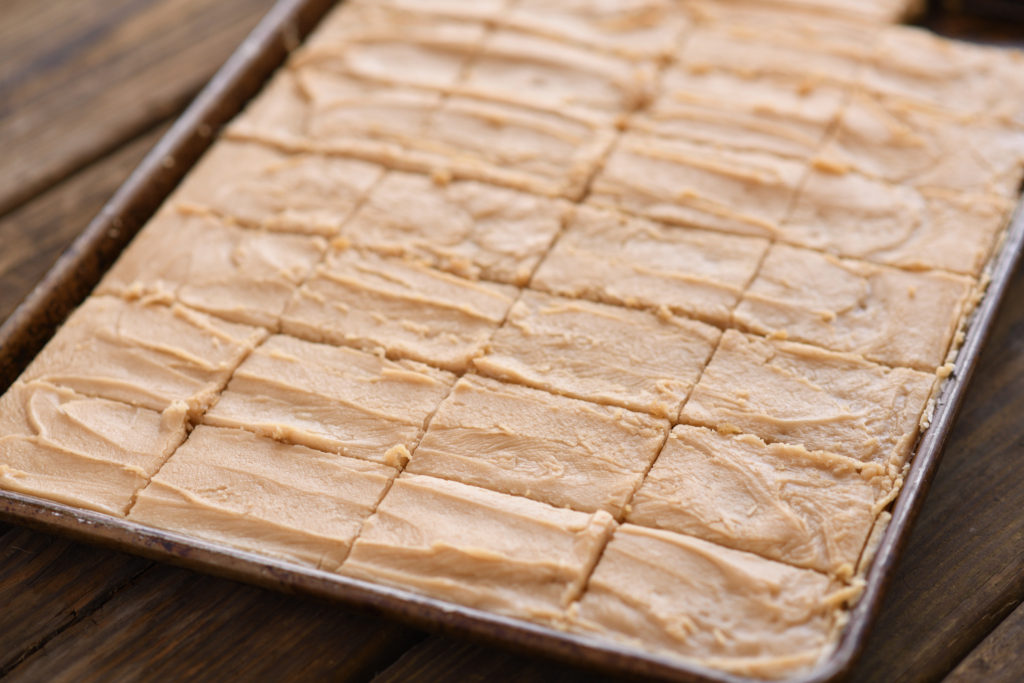 A pan of fresh baked peanut butter sheet cake with peanut butter fudge frosting cut into squares