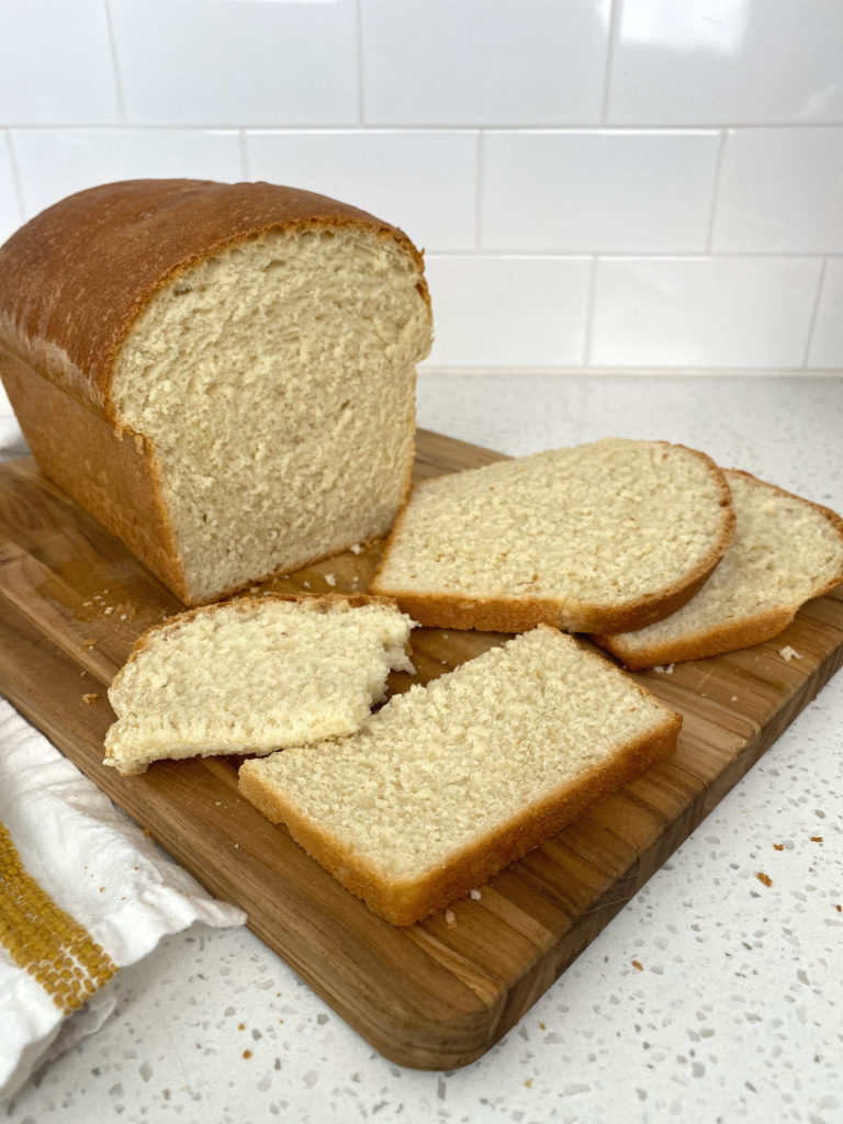 A loaf of buttermilk white bread on a cutting board, cut into slices.