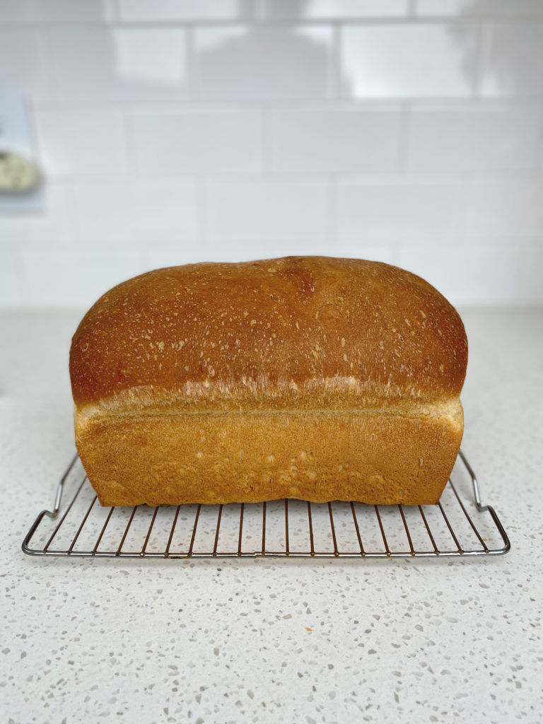 A side view of a fresh baked loaf of buttermilk bread cooling on a wire rack.