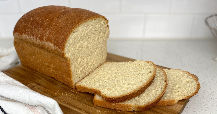 A loaf of Buttermilk White Bread on a cutting board cut into slices.