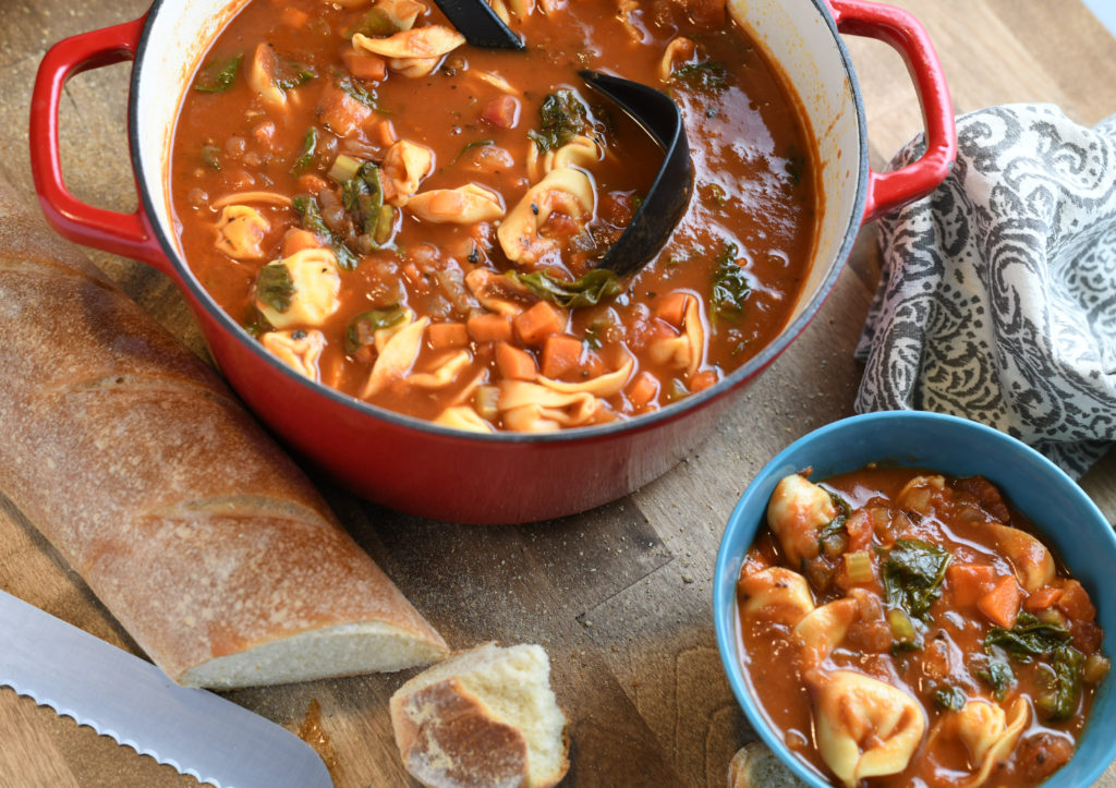 A pot of tortellini soup and a bowl of soup next to it.